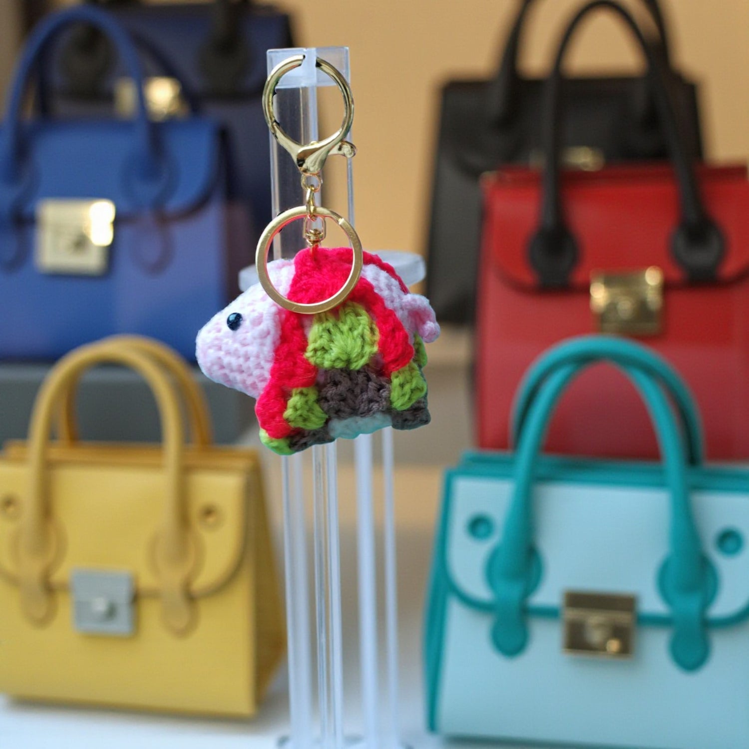 Colorful Crochet Pig Key Ring with a in front of a shop window display of blurred handbags