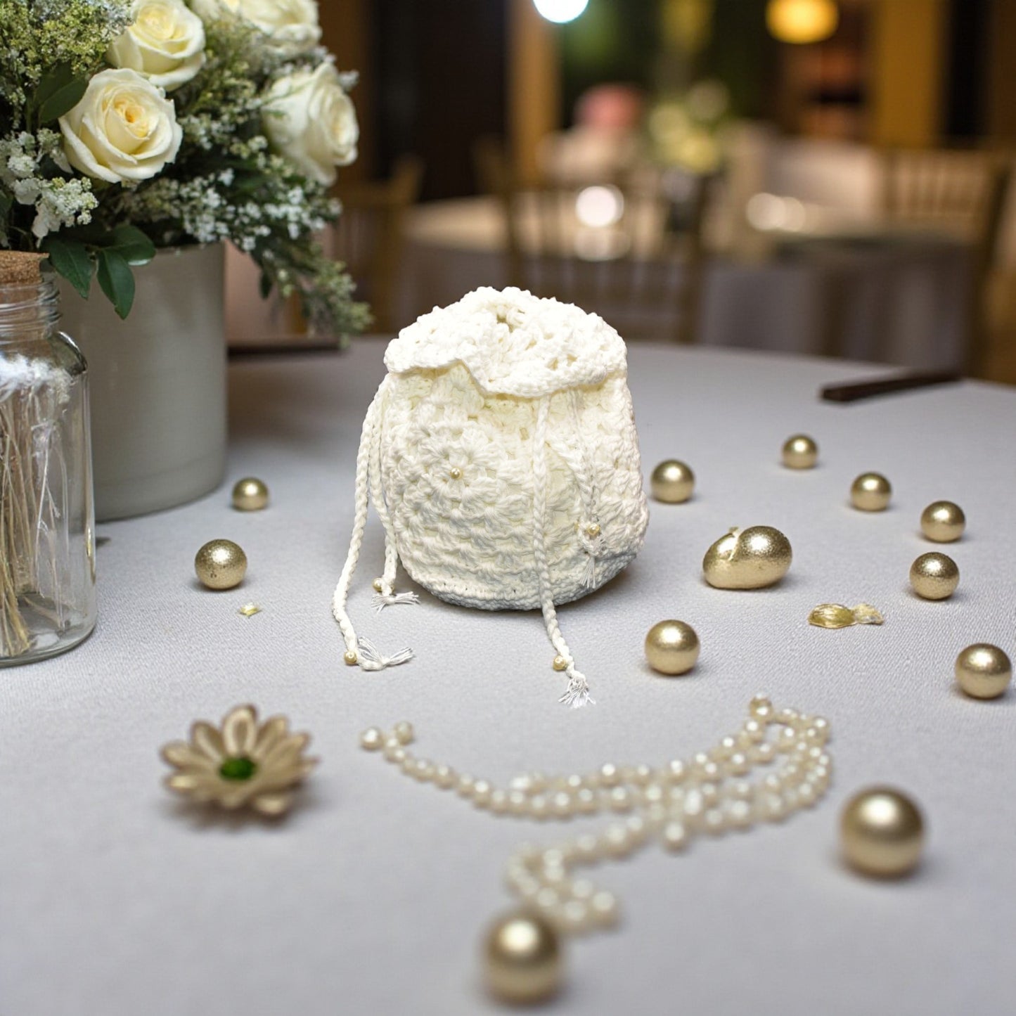 Decorative white wedding lace bag with pearls on a table with gold jewelry and flowers.