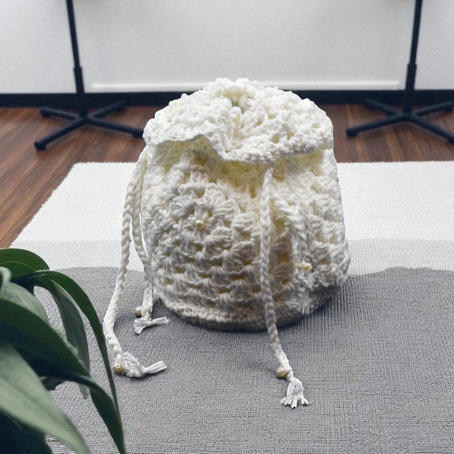 White crochet bag on a gray surface with a plant in the foreground