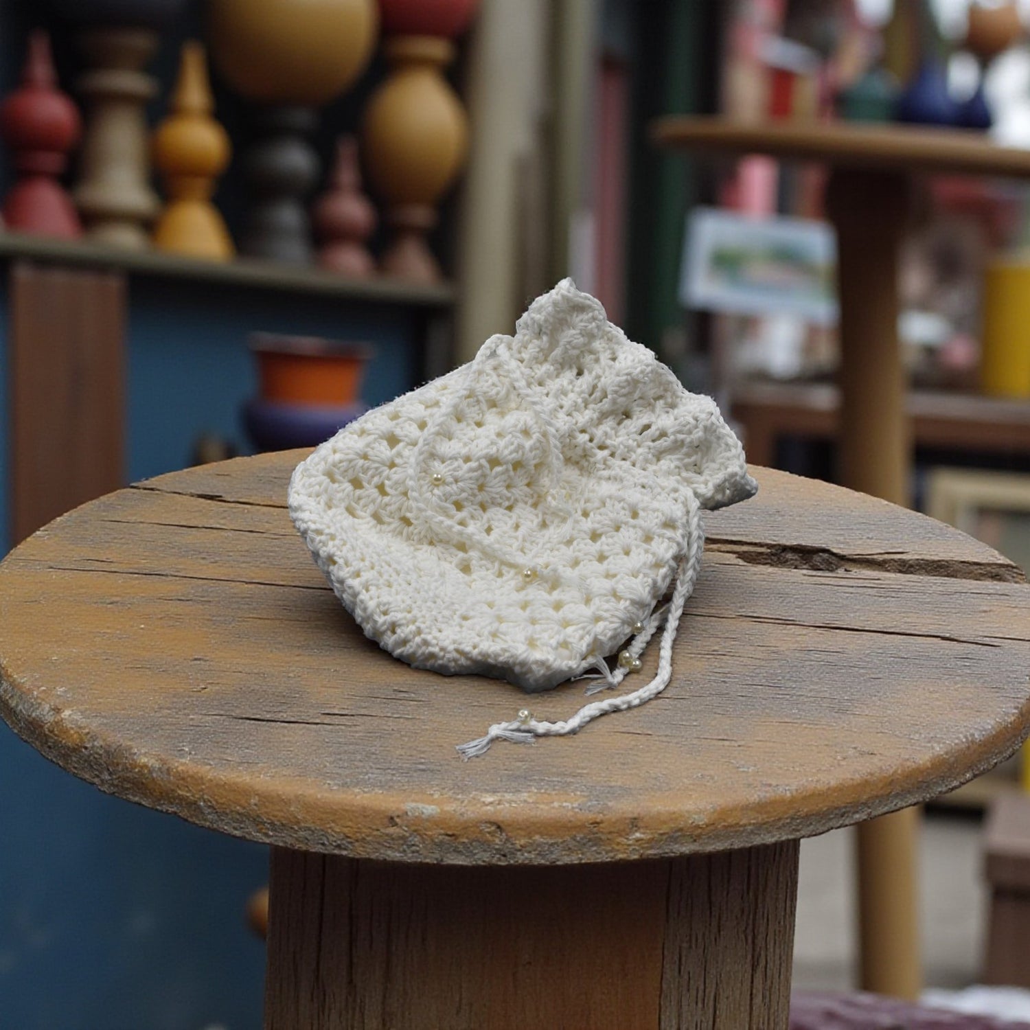 White drawstring crochet bag on a wooden surface with a blurred shop background
