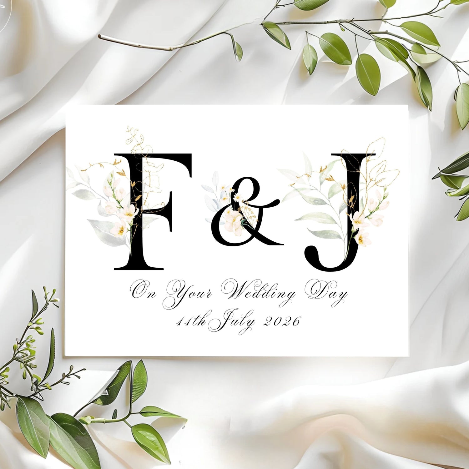 Wedding card with initials 'F' & 'J' and floral design on a white fabric background.