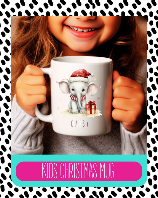 A child holding a white ceramic mug with a Christmas themed design featuring an elephant, gifts, and the text 'Kids Christmas Mug'.