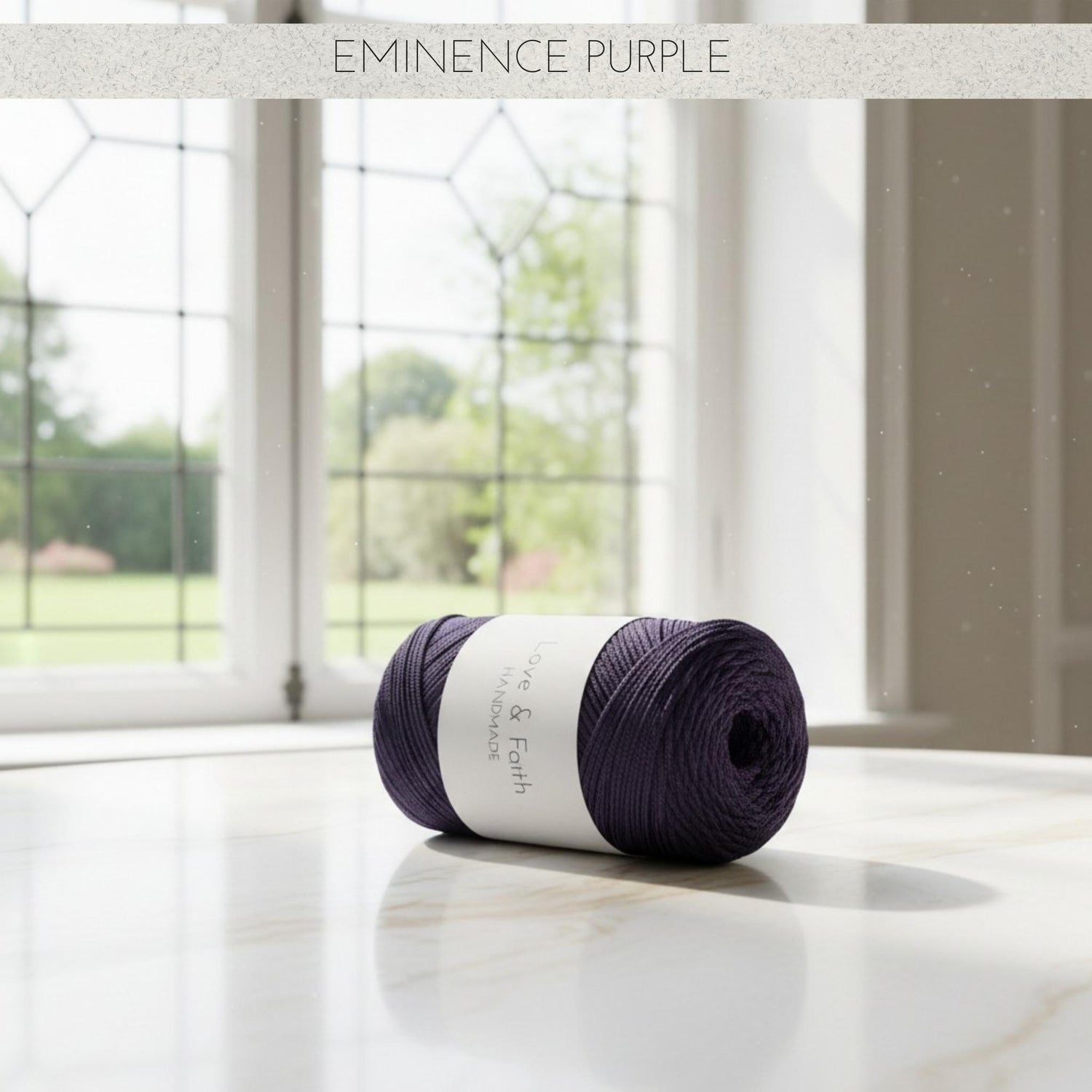Ball of yarn labelled 'Eminence Purple' on a marble surface with a window in the background