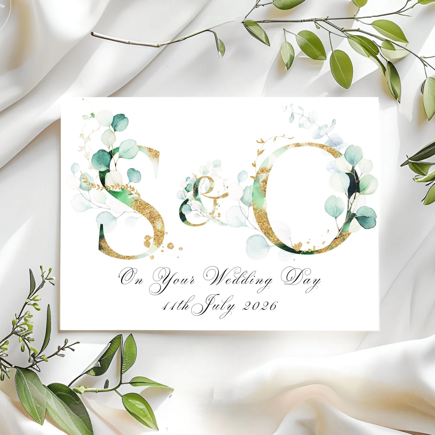 Wedding card with initials 'SO' and greenery on a white fabric background
