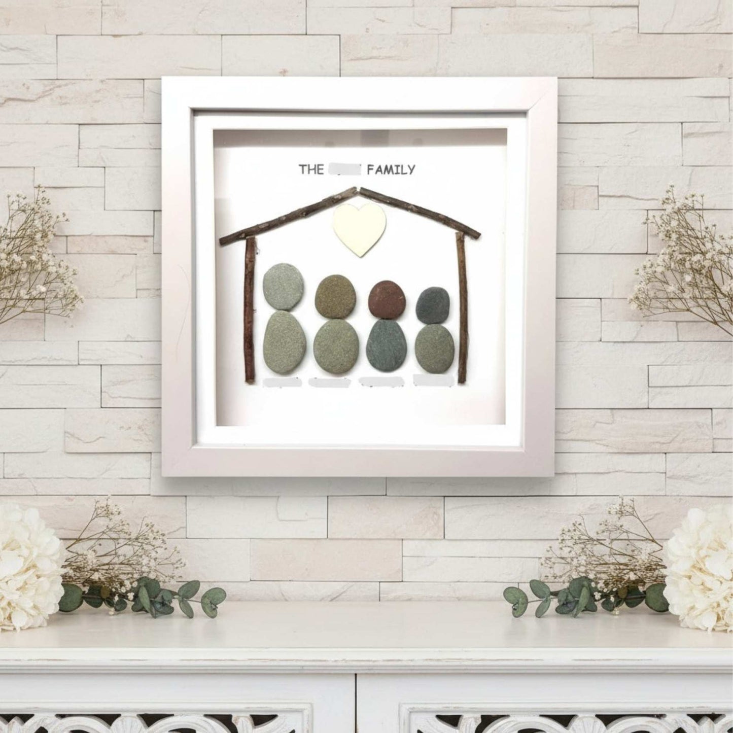 Framed artwork with pebble family design on a light wooden wall.