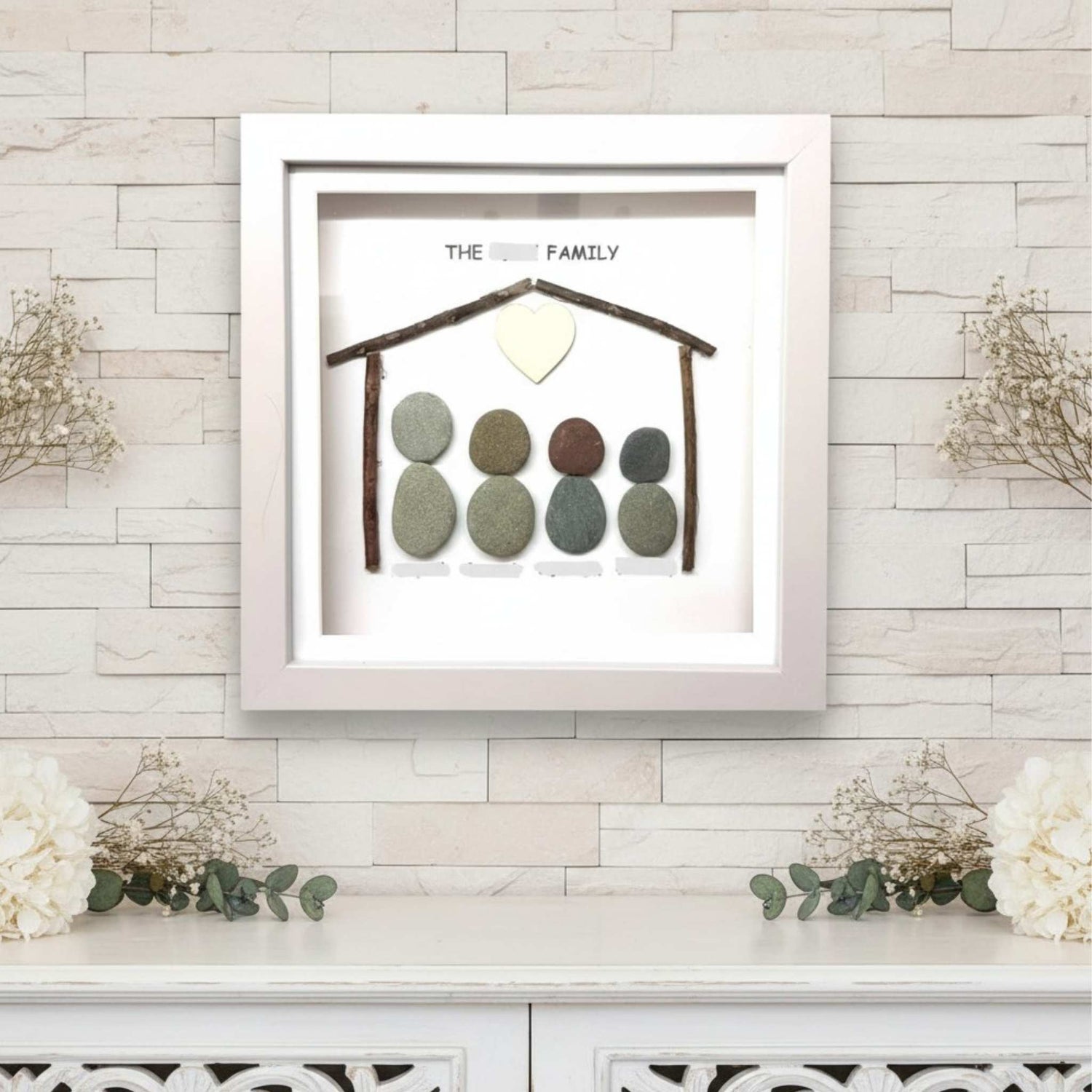 Framed artwork with pebble family design on a light wooden wall.