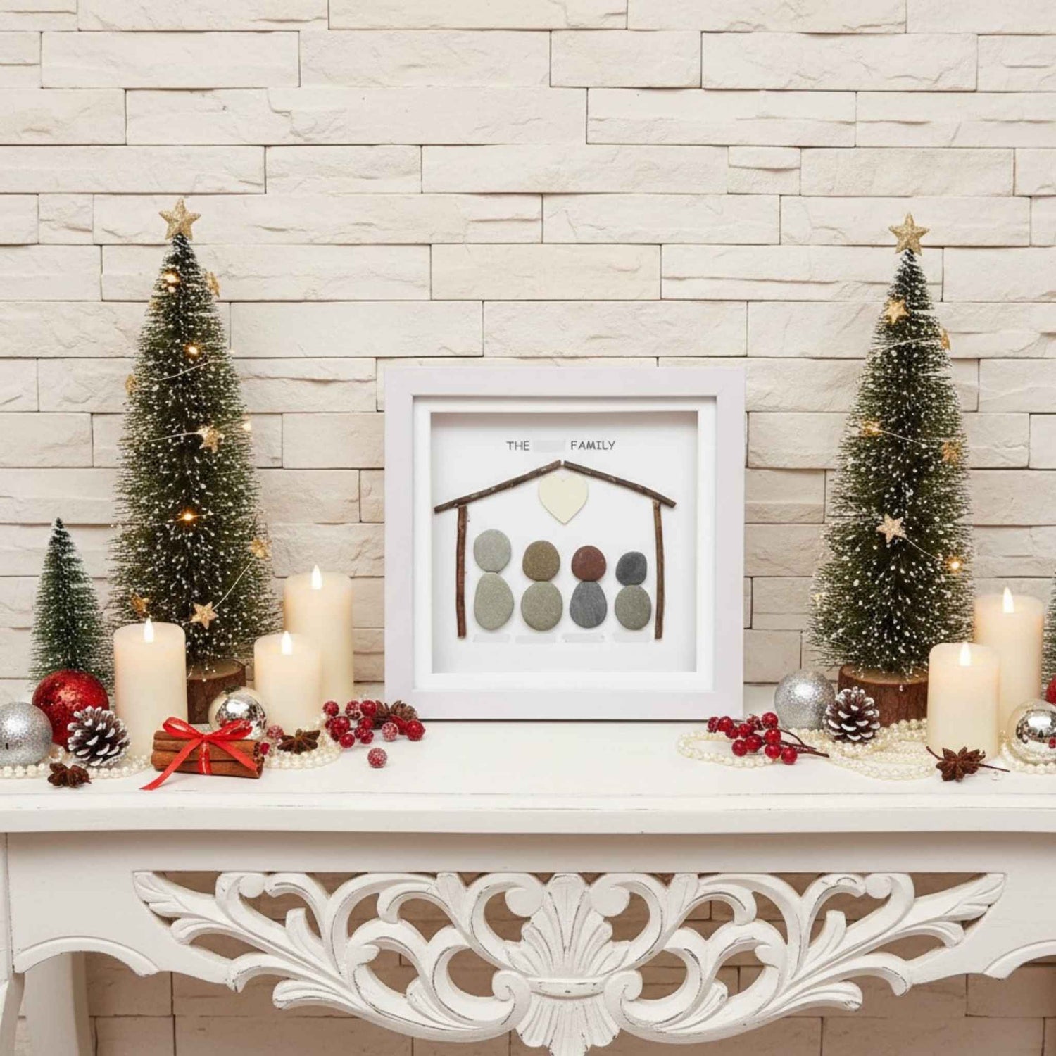Decorative Christmas mantel with framed pebble artwork, candles, and small trees against a stone wall.