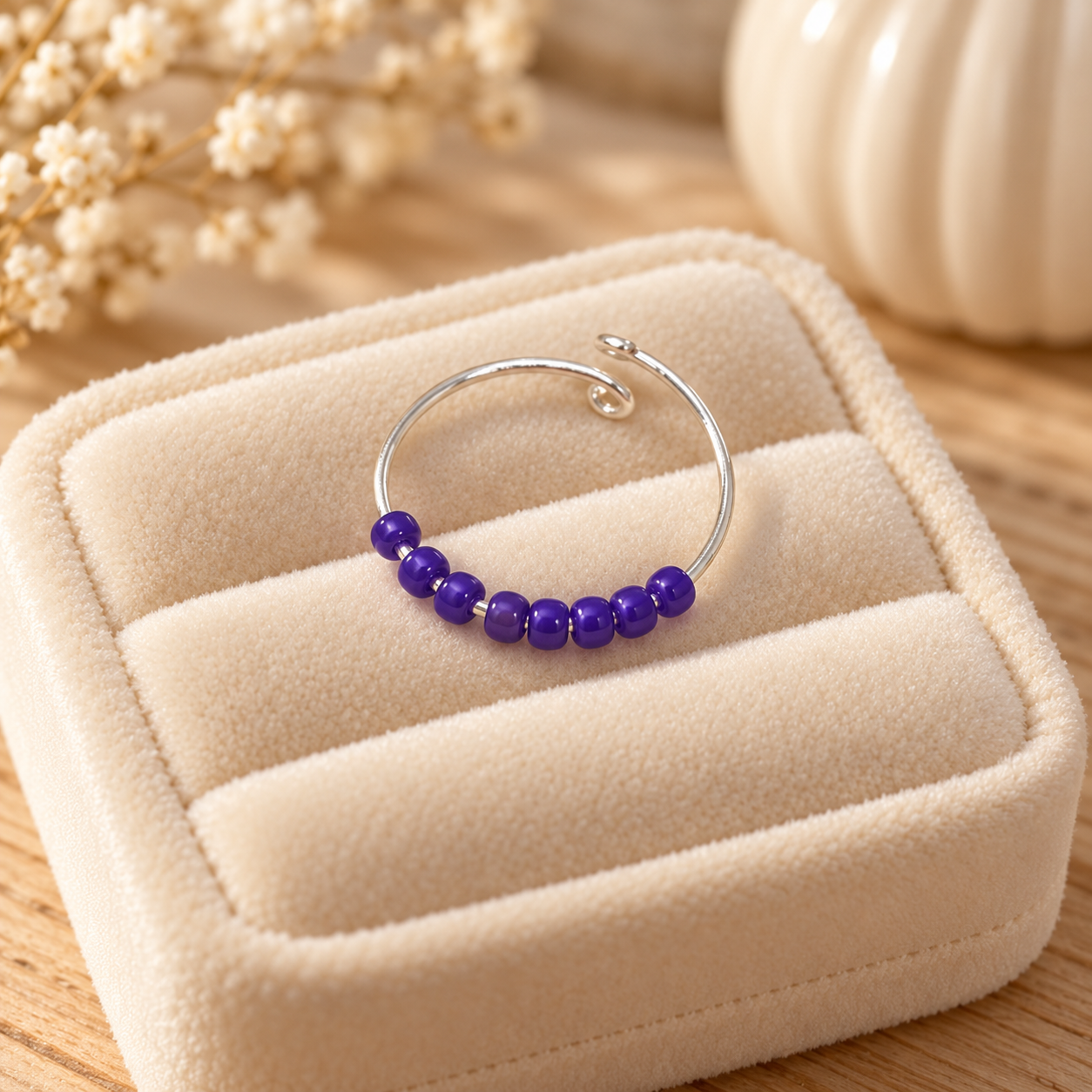 A silver-tone open fidget ring with a row of small purple beads, displayed on a beige velvet jewellery box.