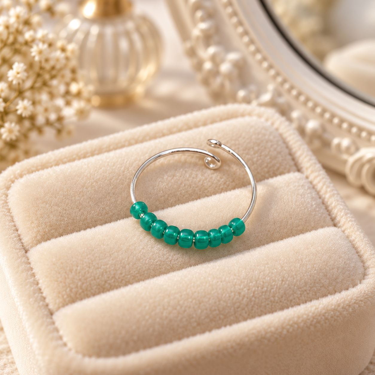 A silver fidget ring with a row of glossy green beads, displayed on a beige velvet jewellery box.