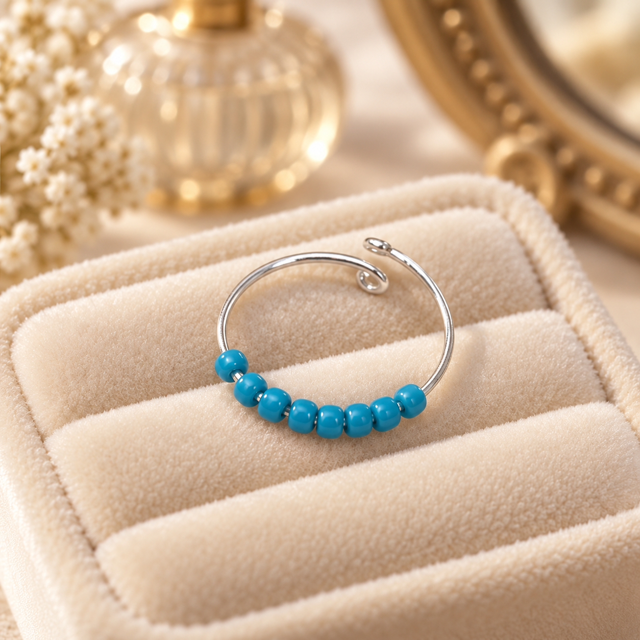 A silver-toned open fidget ring with a row of small turquoise-blue beads, displayed on a cream-coloured jewellery pouch