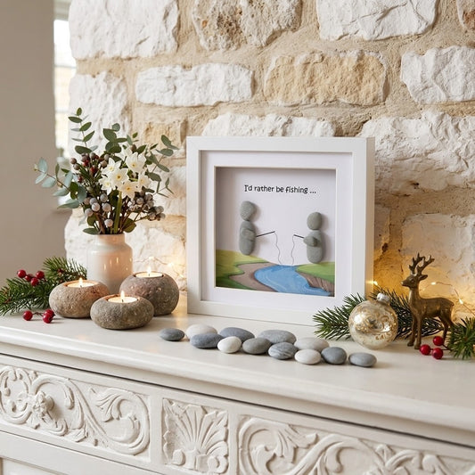A white framed art print on a mantelpiece, featuring a landscape illustration of a river and pond with the text 'I'd rather be fishing.