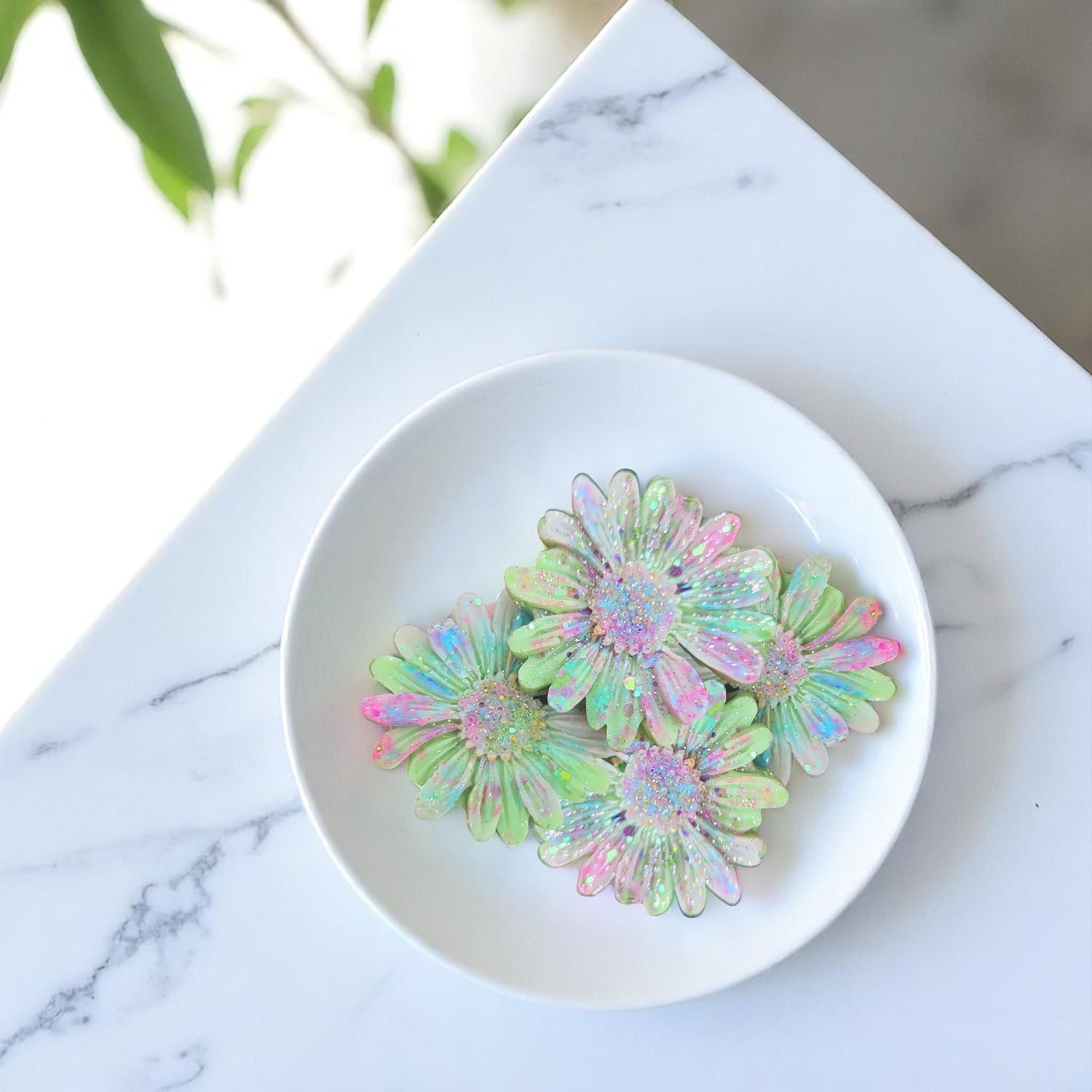 Iridescent flower-shaped wax melts on a white plate with a marble background