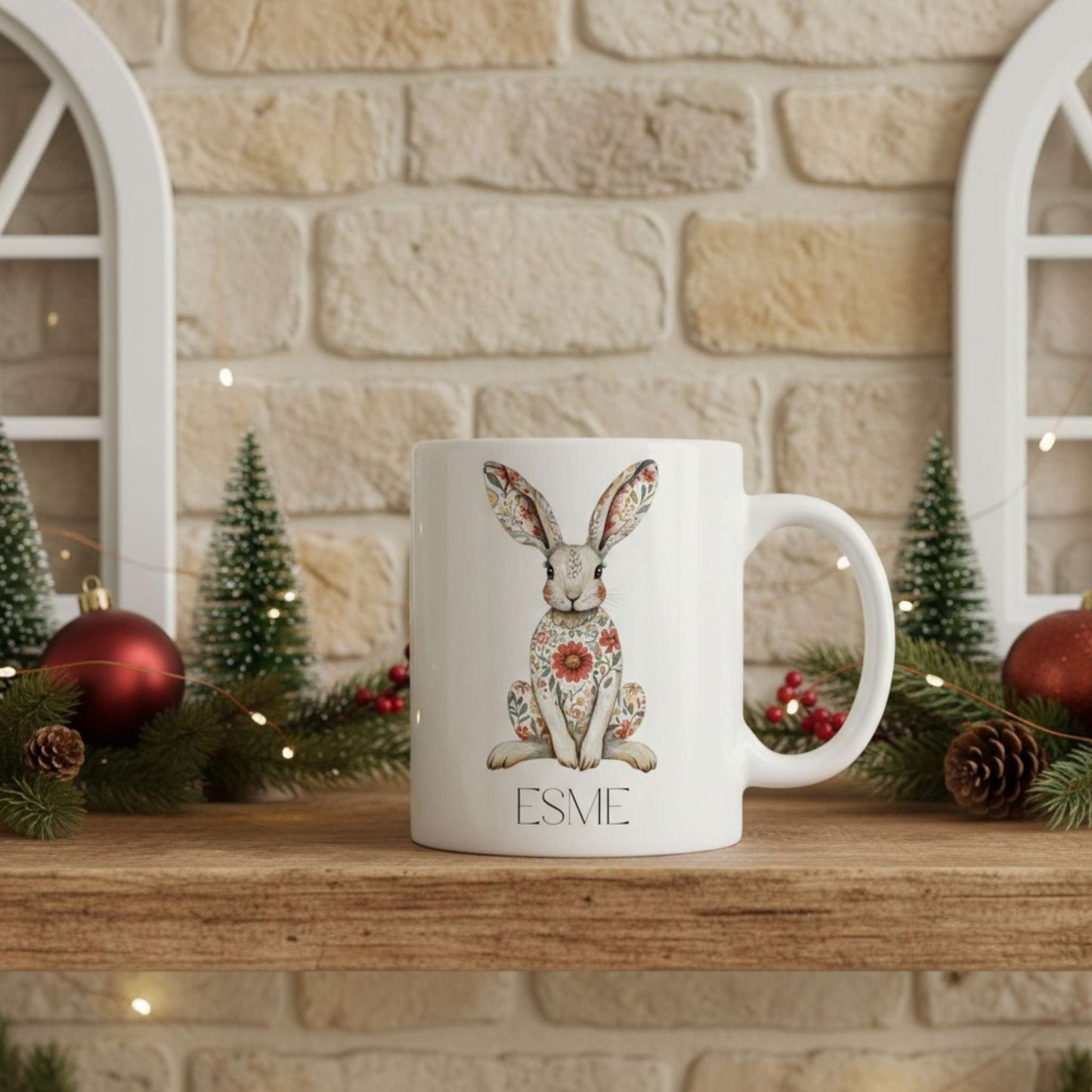 White mug with a hare design and 'ESME' text on a wooden surface with festive decorations.