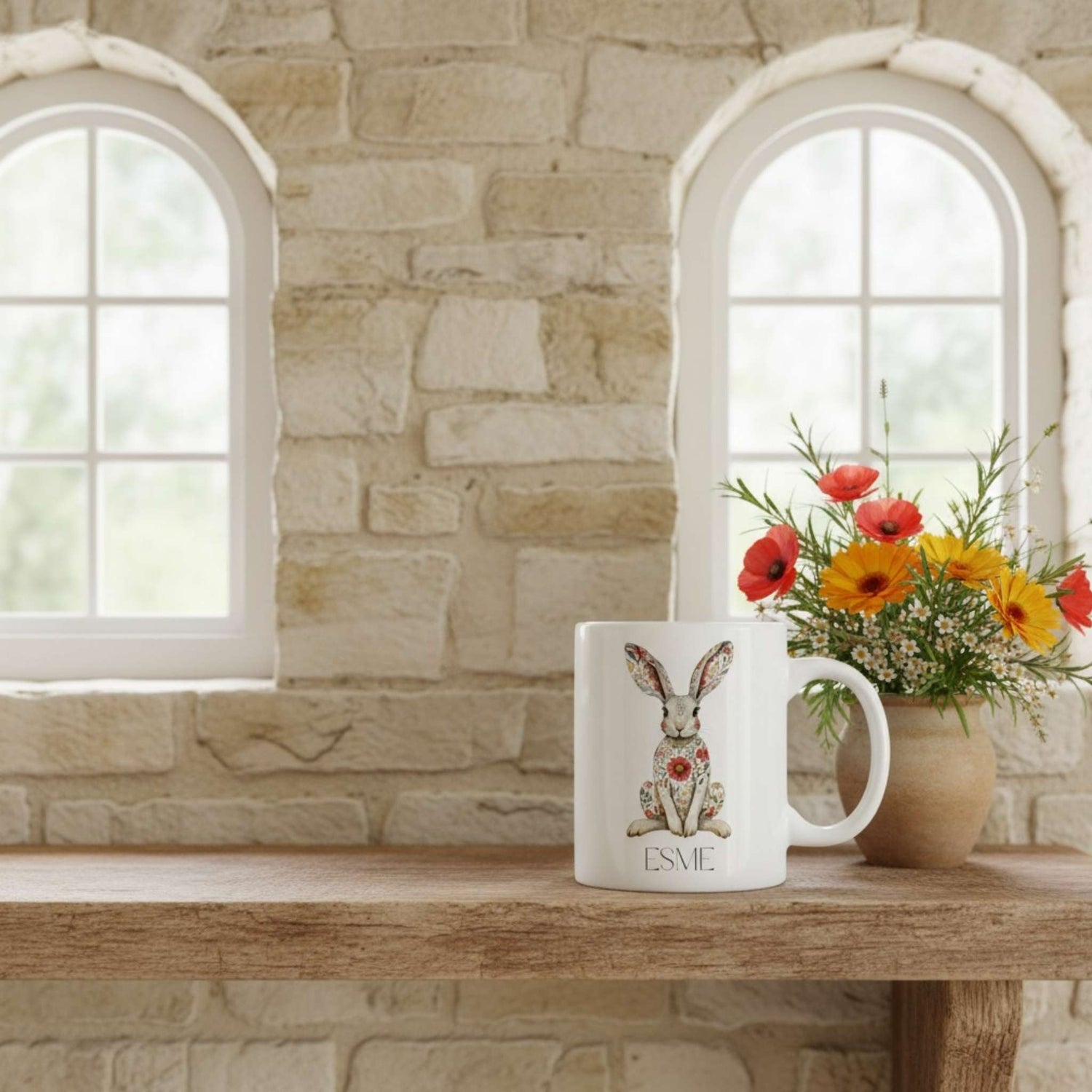 Mug with a rabbit hare and floral patterns on a wooden surface with a stone wall background