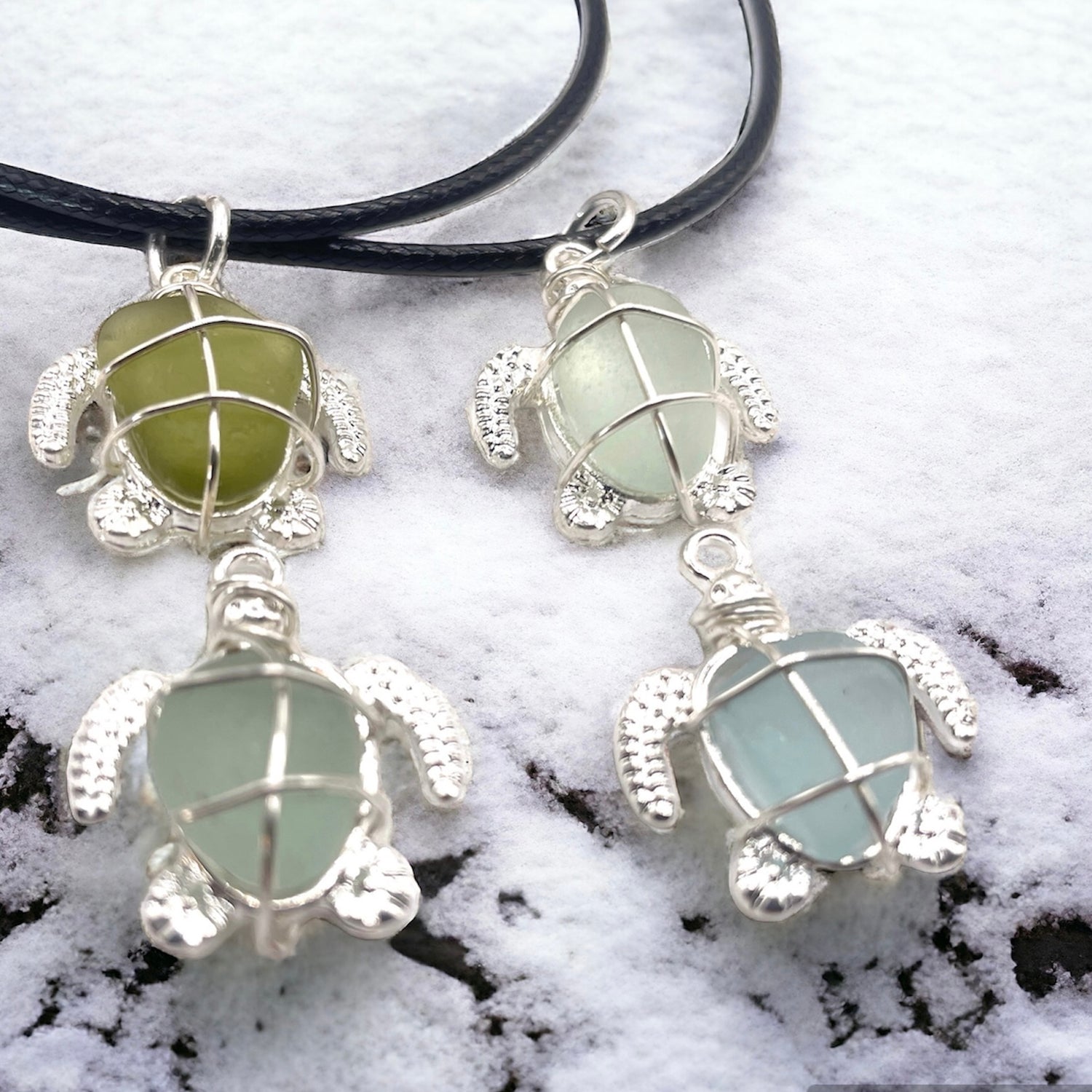 Four sea glass turtle pendants with sea glass on a snowy background.