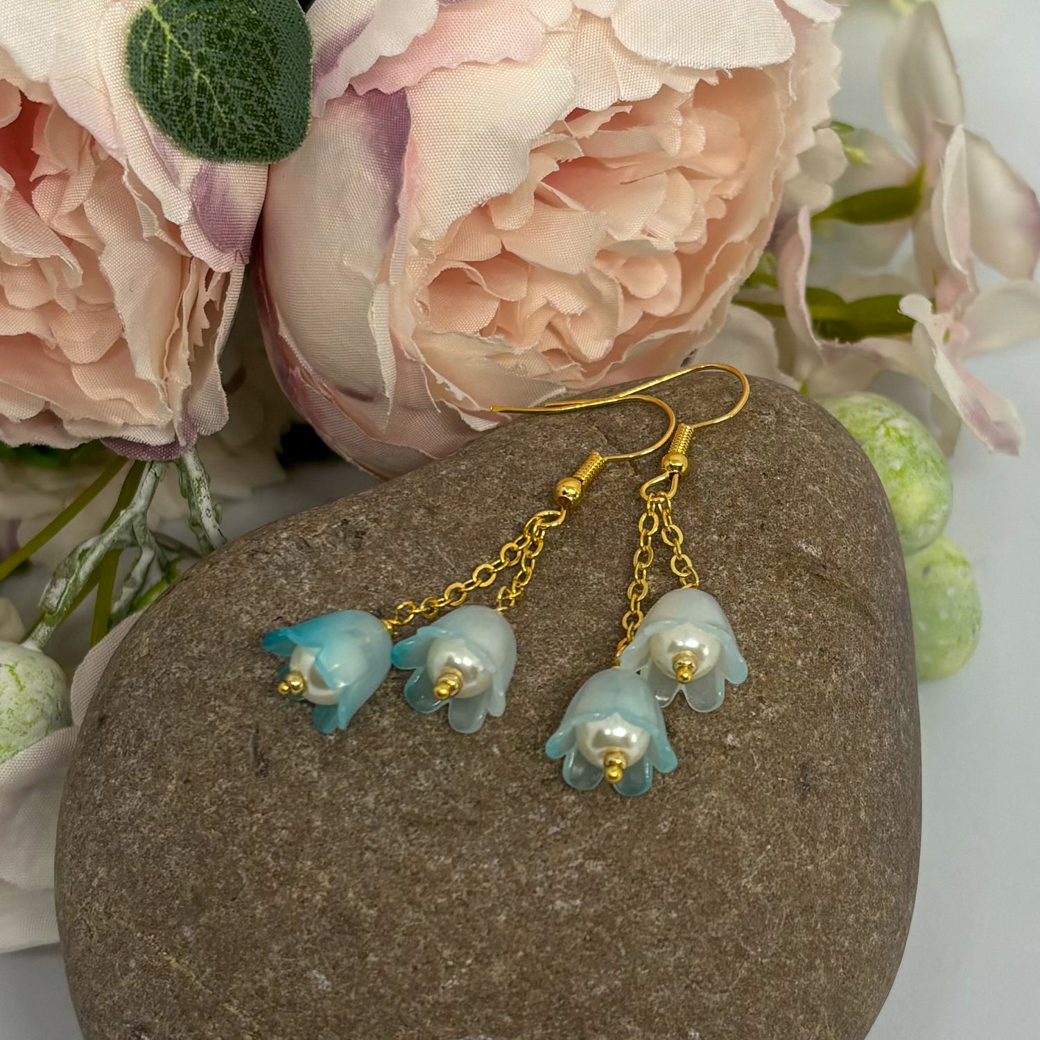 frosted blue earrings with gold hooks on a stone with flowers
