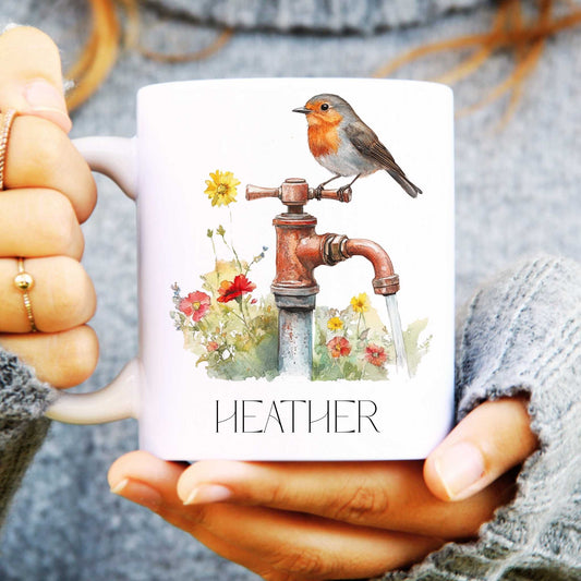 Mug with a design of a robin on a faucet and flowers, held by a person wearing a textured sleeve.