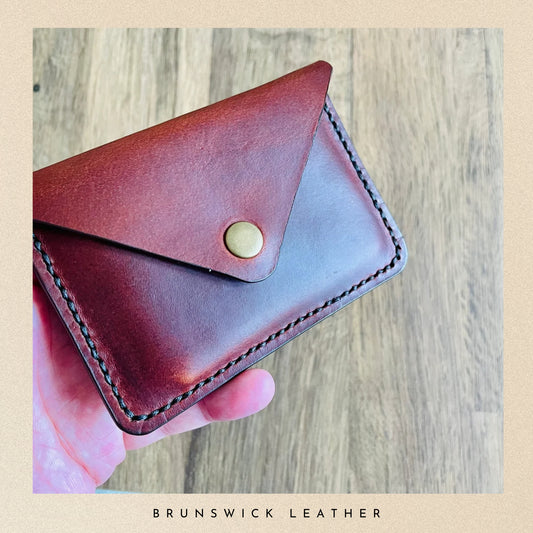 Brown leather wallet held by a hand on a wooden surface with 'Brunswick Leather' branding.
