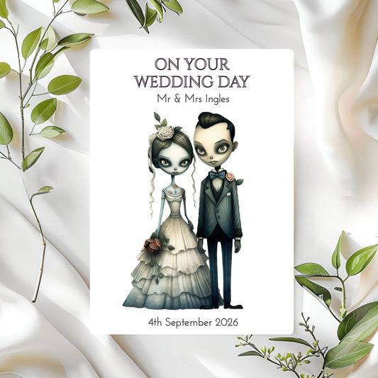 Wedding card with gothic bride and groom on a white fabric background with green leaves.