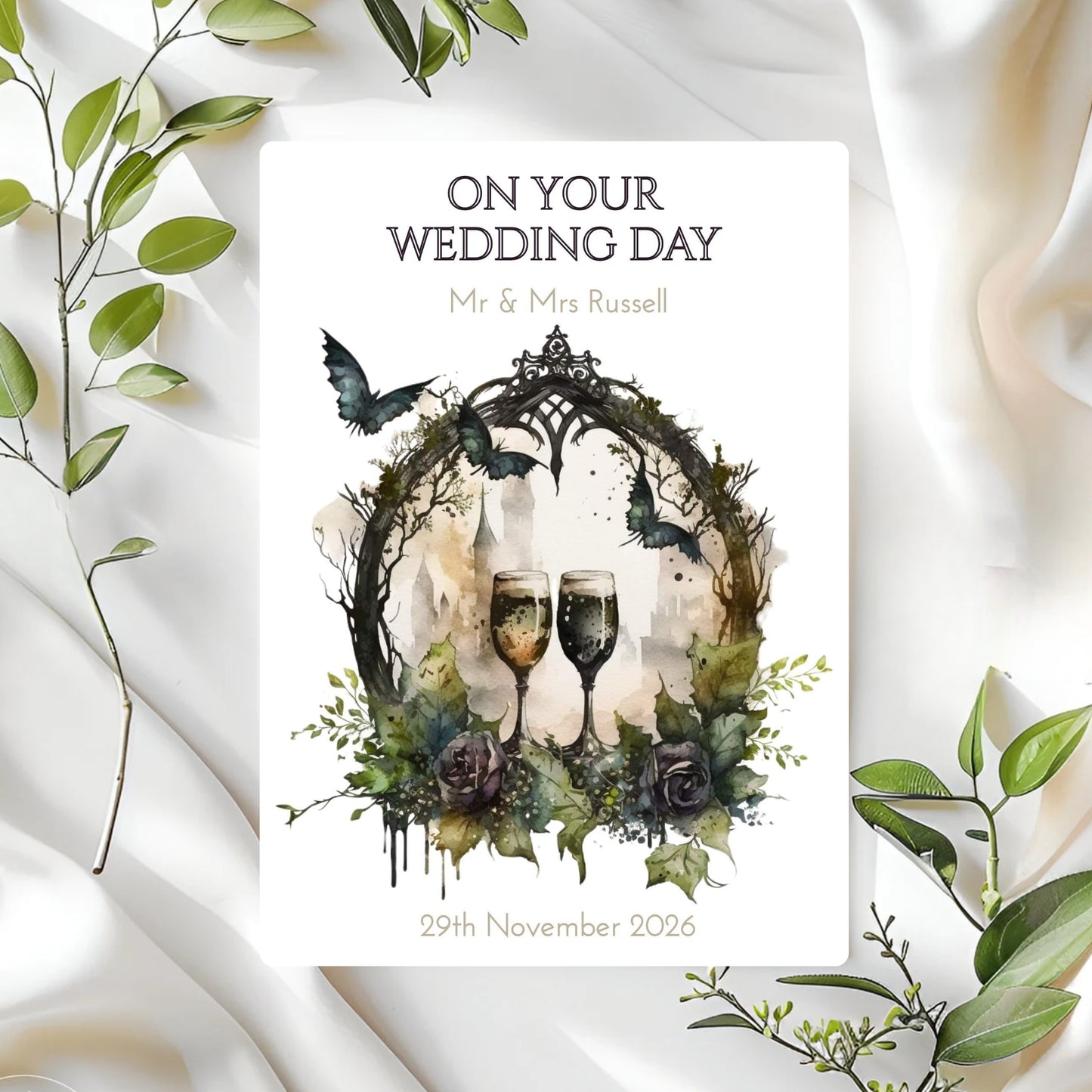 Gothic Wedding card with wine glasses, flowers, and text on a white fabric background