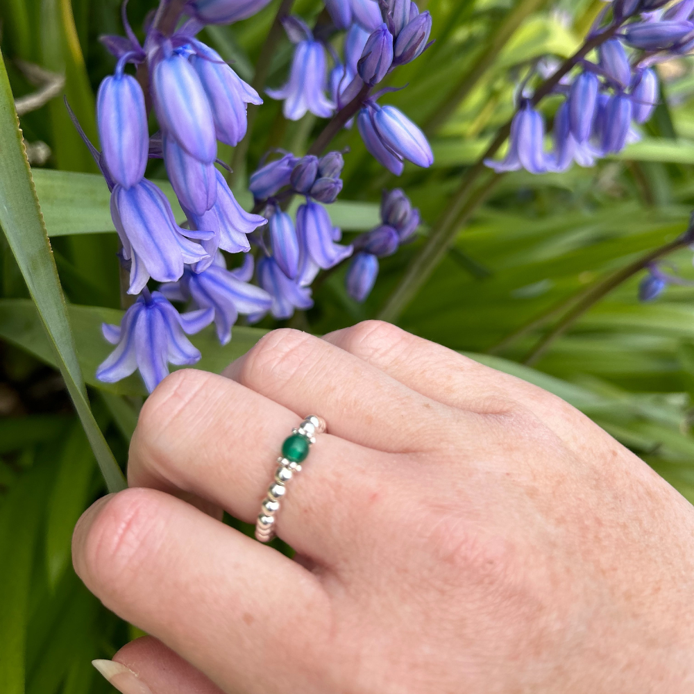 A hand wearing a sterling silver bead agate ring with green agate bead and two silver daisy spacers.