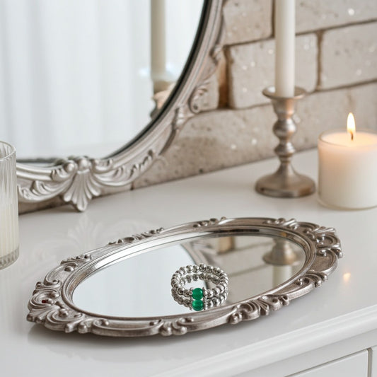 Silver ornate mirror with a green agate ring on a white surface, candles, and a decorative mirror in the background.