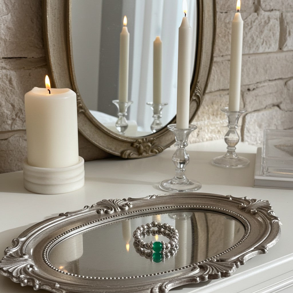 Decorative setup with candles, a mirror, and a silver tray with green agate ring on a stone surface.