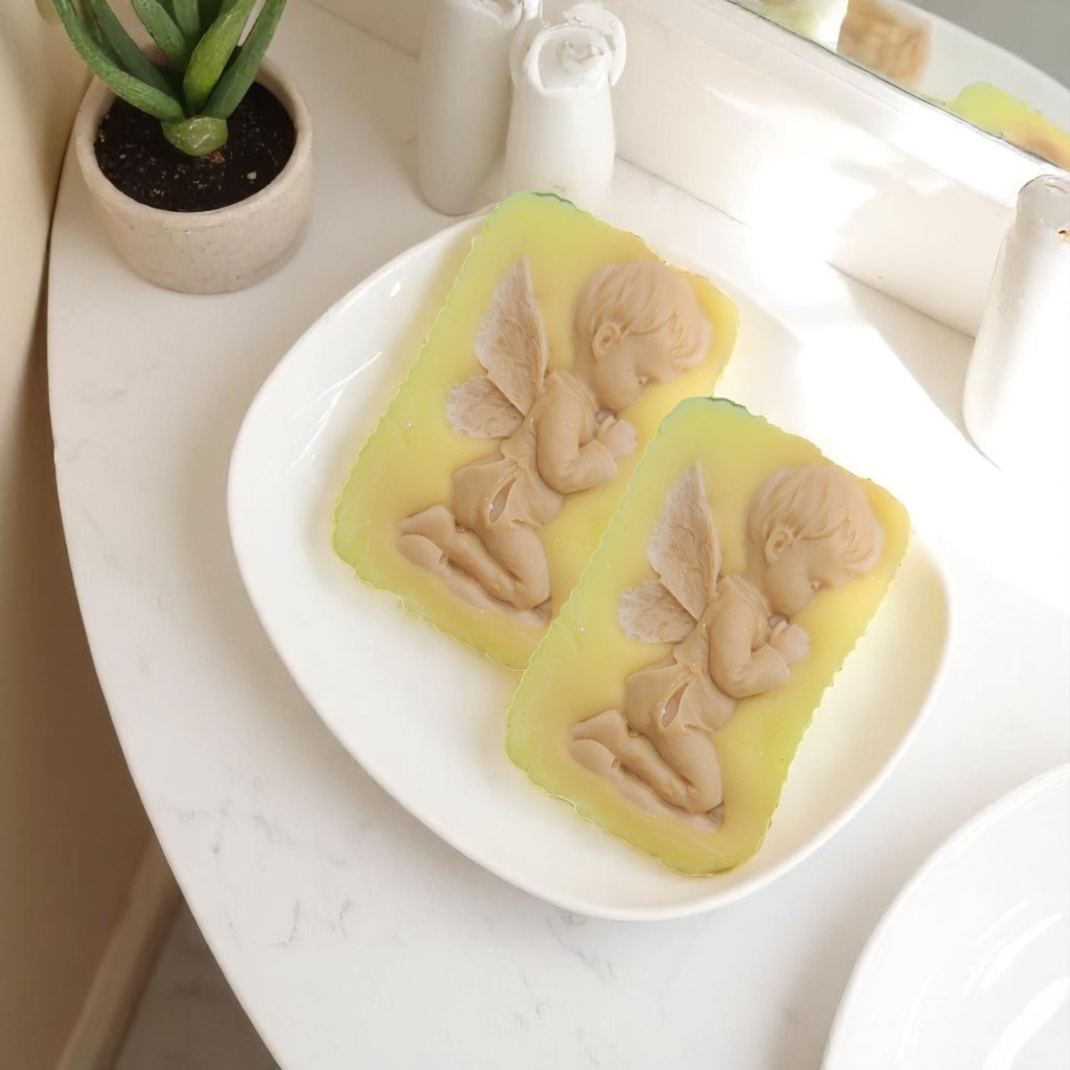 Two yellow wax melt bars with butterfly designs and cherub on a white plate, placed on a light surface.
