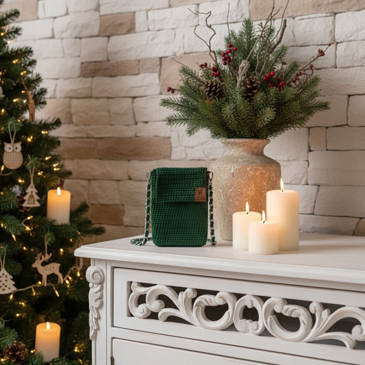 Decorative setting with a Christmas tree, candles, and a vase with greenery on a white cabinet against a stone wall.