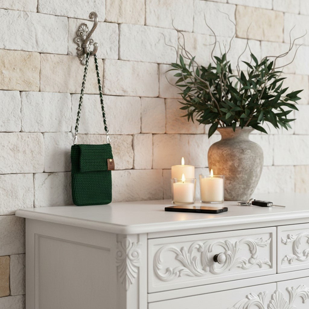 Decorative setting with a green bag, candles, and a vase on a white cabinet against a stone wall.