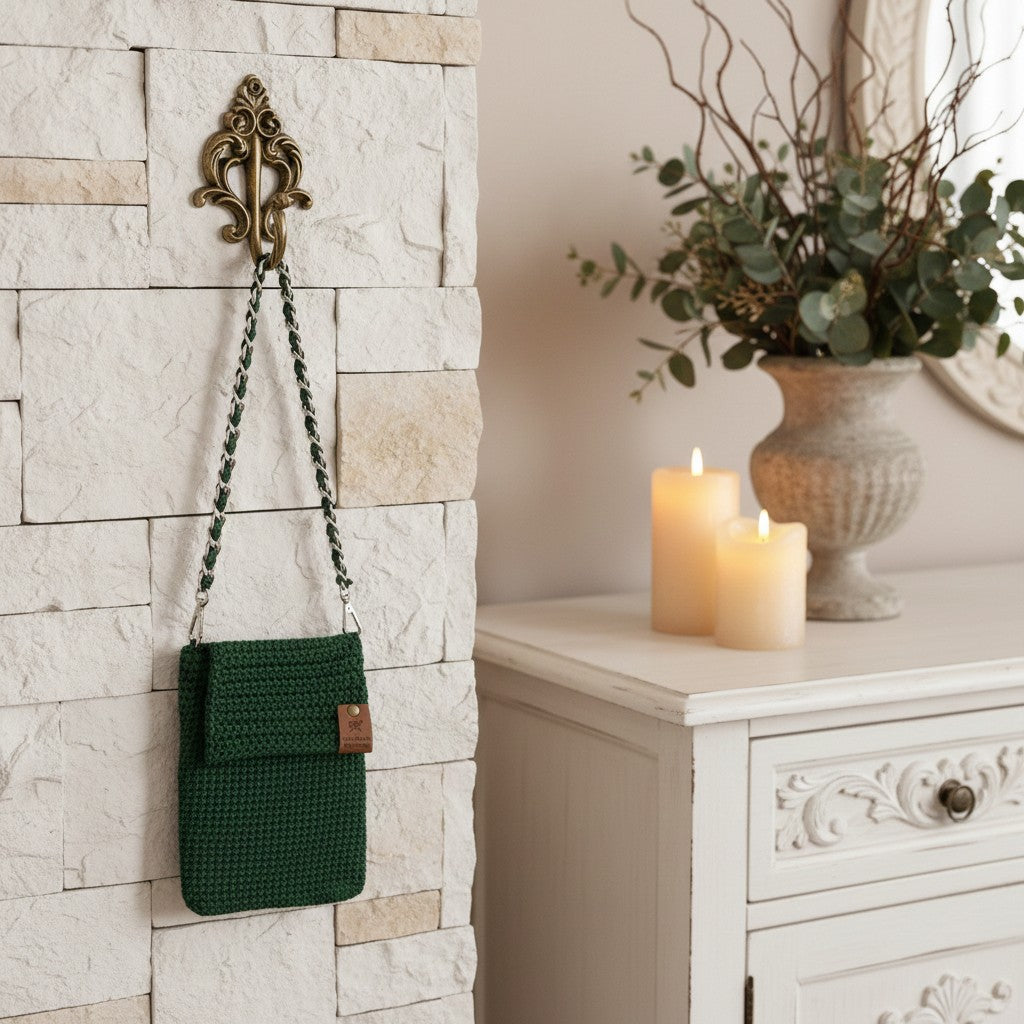 Green woven bag hanging on a decorative wall hook next to a white cabinet with candles and a vase.