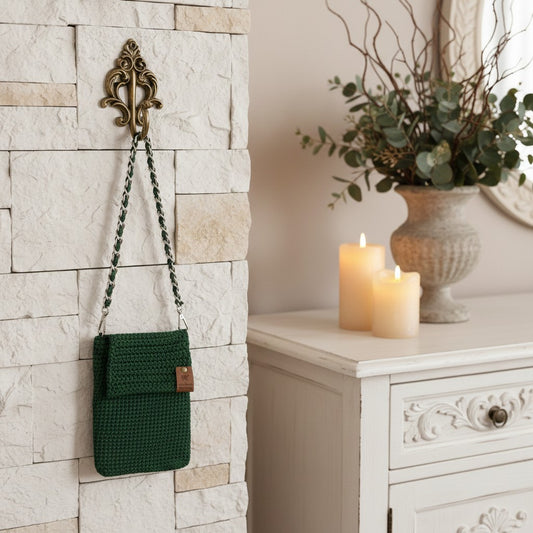 Green woven bag hanging on a decorative wall hook next to a white cabinet with candles and a vase.