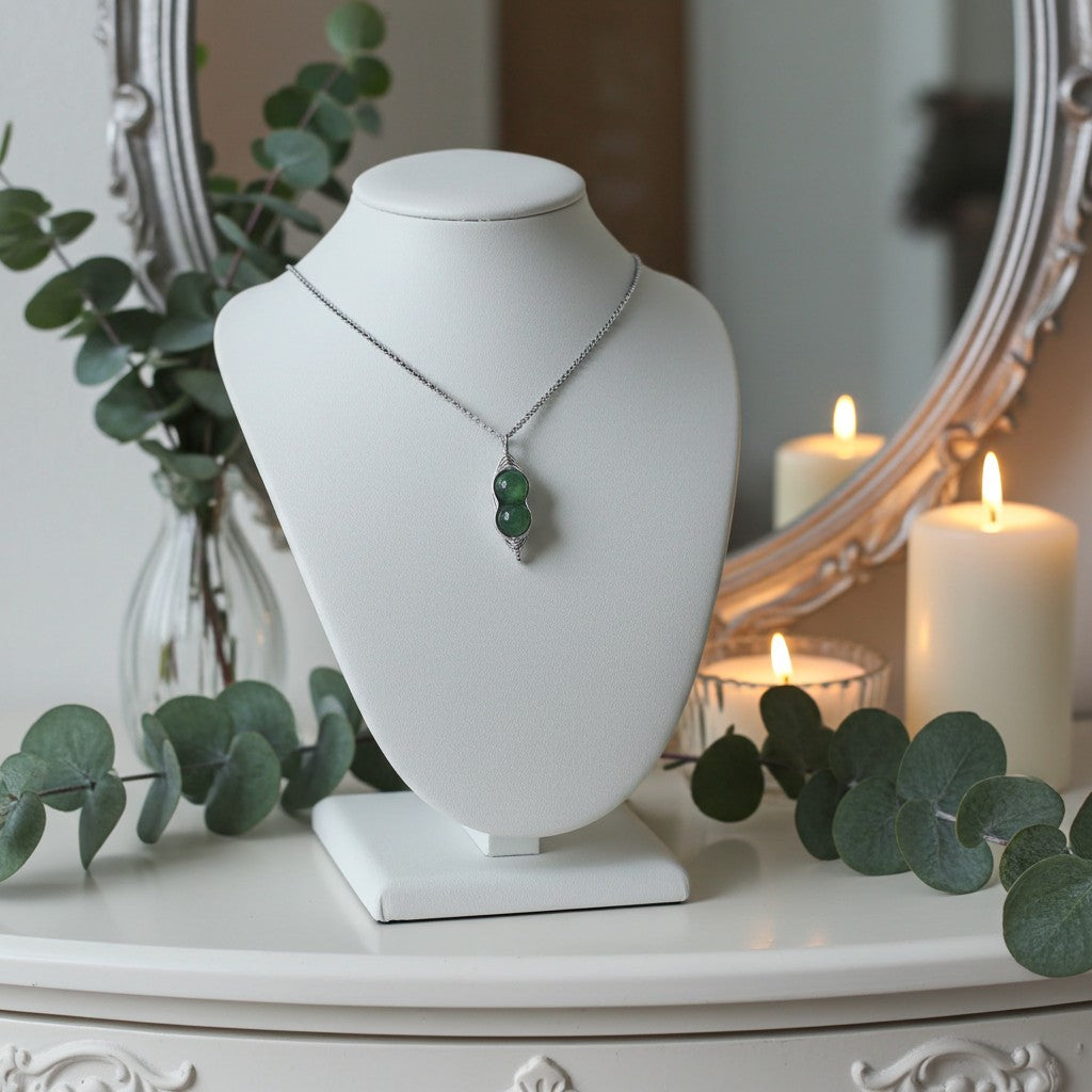 Necklace with green beads on a white mannequin bust in a decorative setting with candles and eucalyptus leaves.