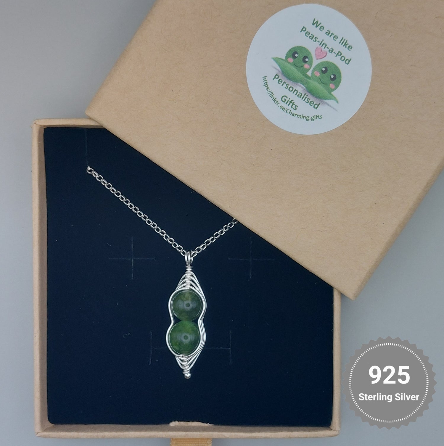 A Green Jade Pea Pod Silver Necklace presented on a printed backing card with a sterling silver clasp, displayed in an open box.