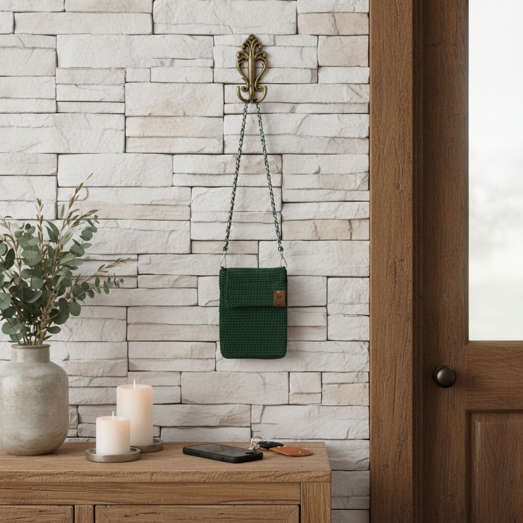 Green bag hanging on a wall hook next to a wooden dresser with candles and a vase.