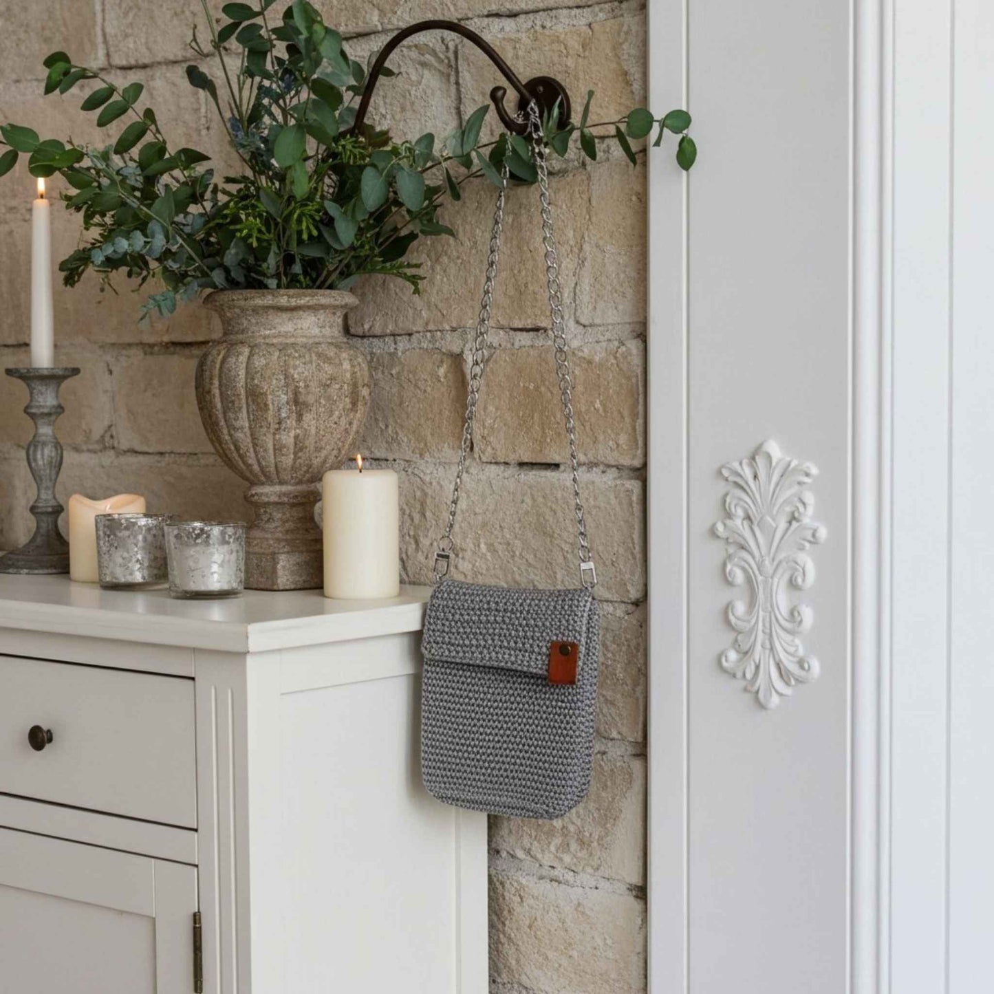 Grey knitted bag hanging on a stone wall with decorative elements.