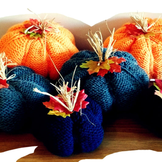 A set of three knitted pumpkin decorations in orange, Blue, and yellow, displayed with autumnal background and decorative pumpkin-shaped wooden base.