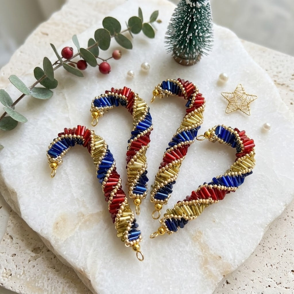 Three handmade beaded candy cane tree decorations in red, white, and blue with gold wire accents, arranged on a white stone slab with holiday decorations.