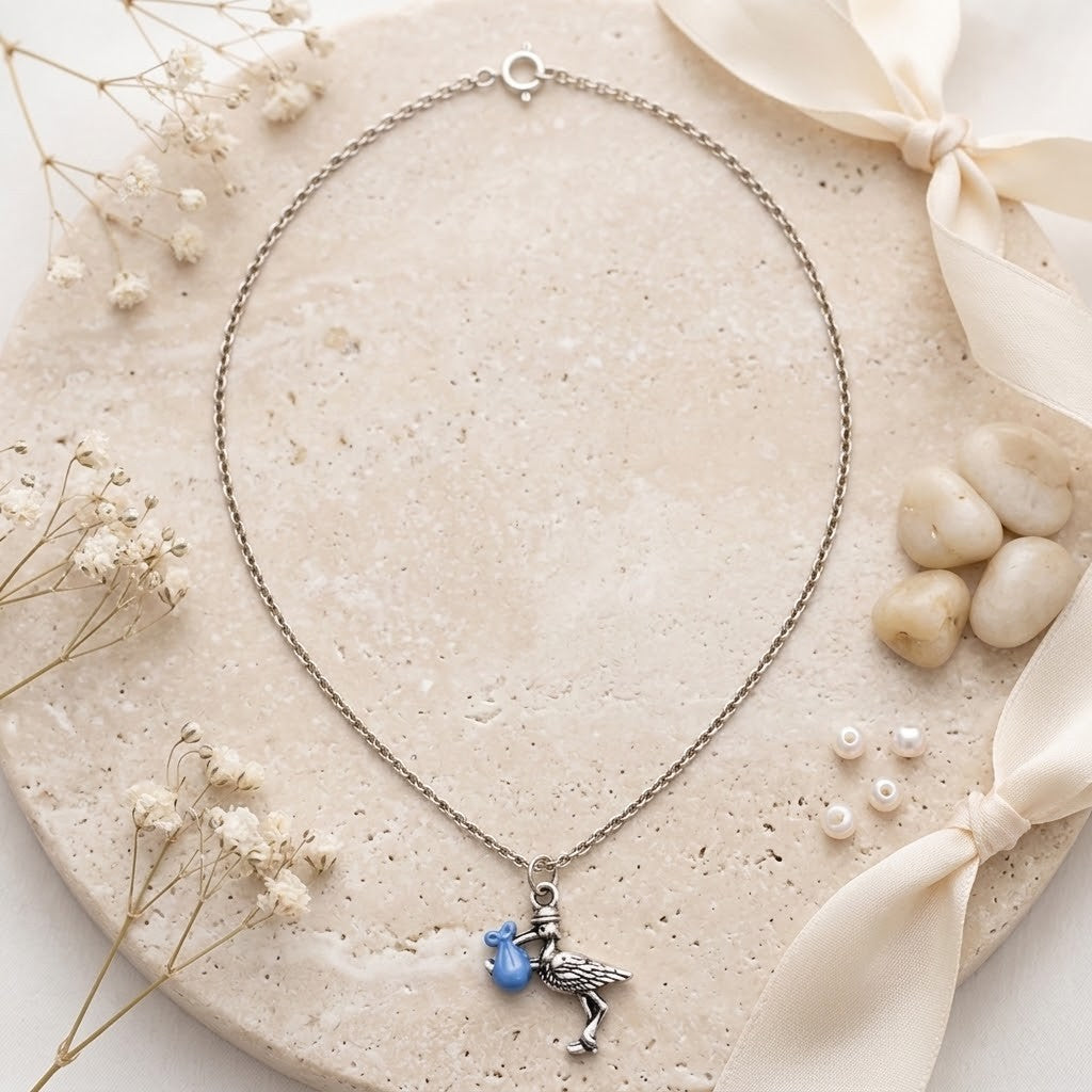 A silver-toned necklace with a stork pendant, displayed on a round beige stone slab with dried flowers, pearls, and cream ribbon.