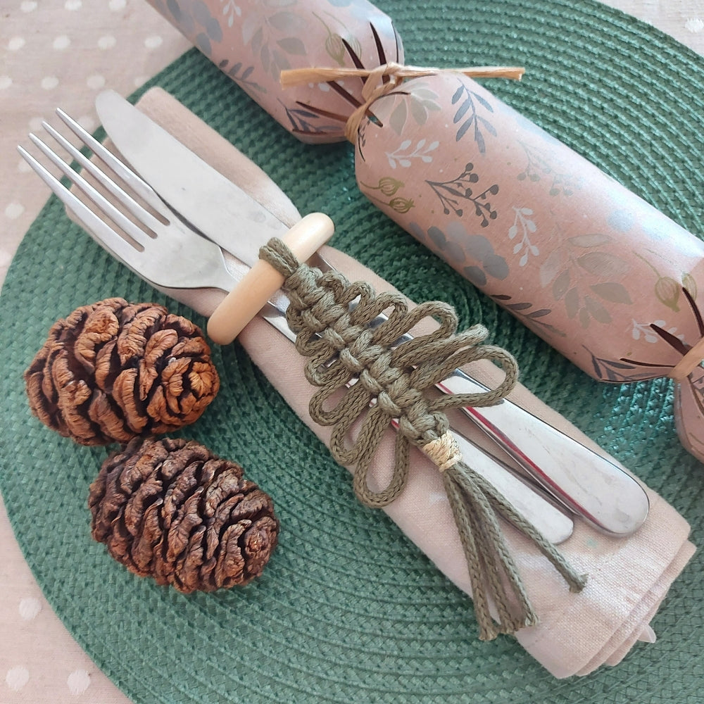 A set of Christmas napkin rings with a green Christmas tree design, placed on a green napkin, with a pine cone and a decorative napkin ring.