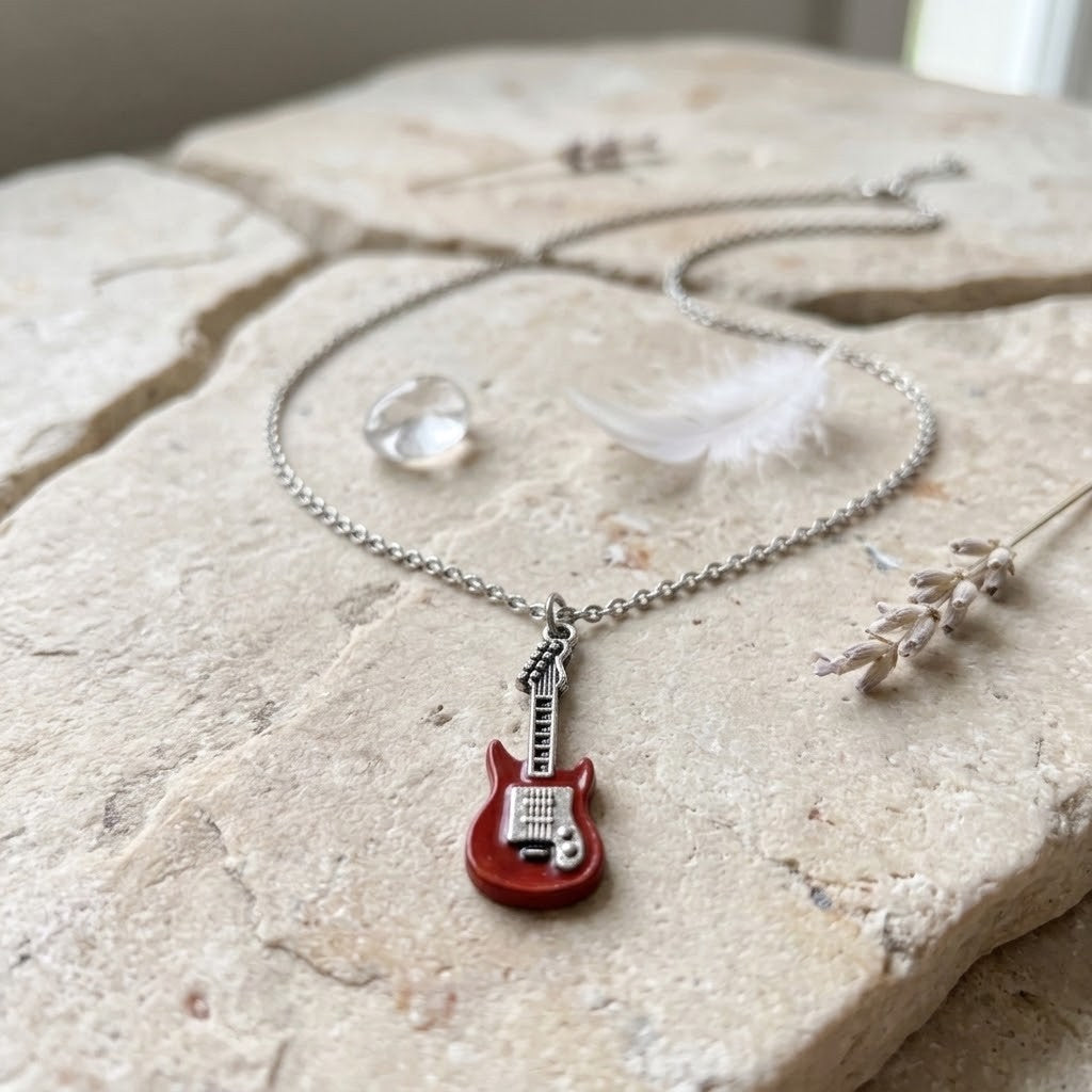 A silver chain necklace with a miniature red electric guitar pendant, styled on a light beige stone surface with a feather, crystal, and dried lavender.