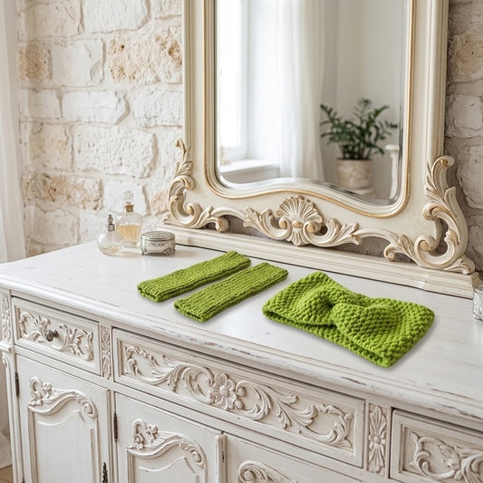 A set of bright green knit accessories, including a large knotted headband and two matching fingerless gloves, displayed on a distressed white wooden console table in front of an ornate cream mirror.