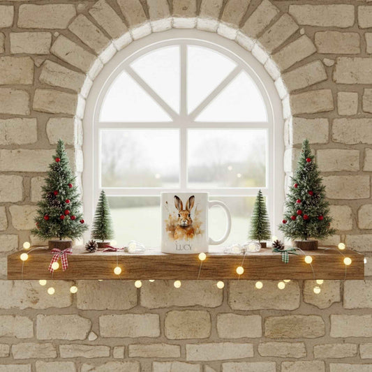 Decorative Christmas mantel with hare mug, small trees, mug, and lights against a stone wall.