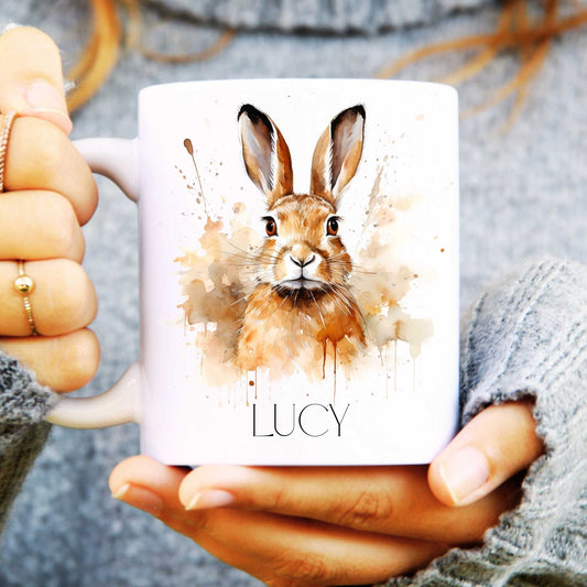 Mug with a hare design and 'LUCY' text held by hands.