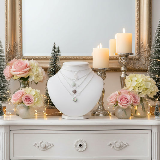 Decorative setting with heart necklaces on jewellery display, candles, and flowers on a white surface.