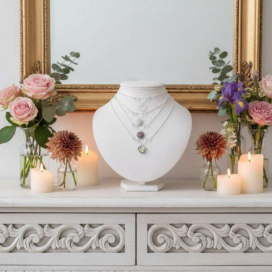 Decorative heart necklace setting with jewellery display, candles, and flowers on a white cabinet.