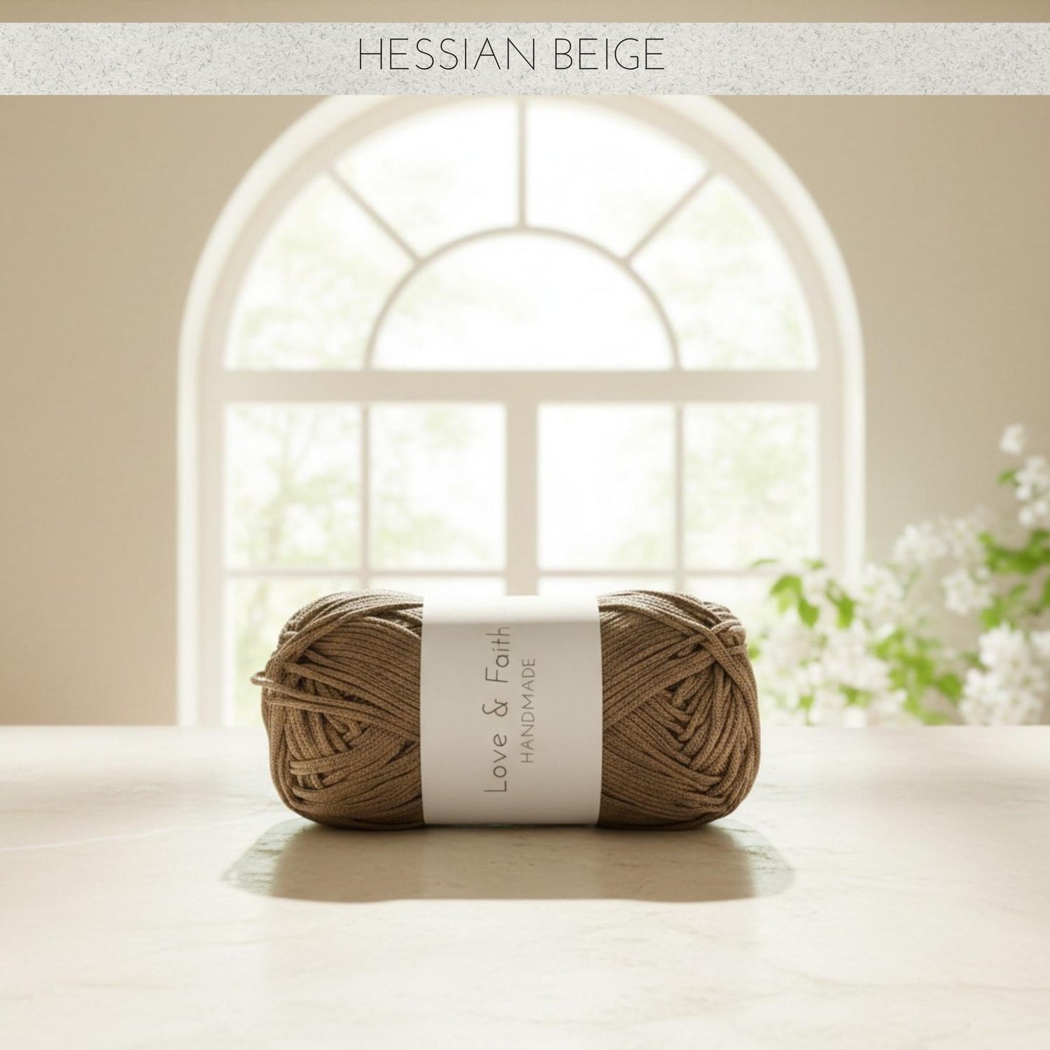 Ball of yarn with a label on a light surface, featuring a window and flowers in the background.