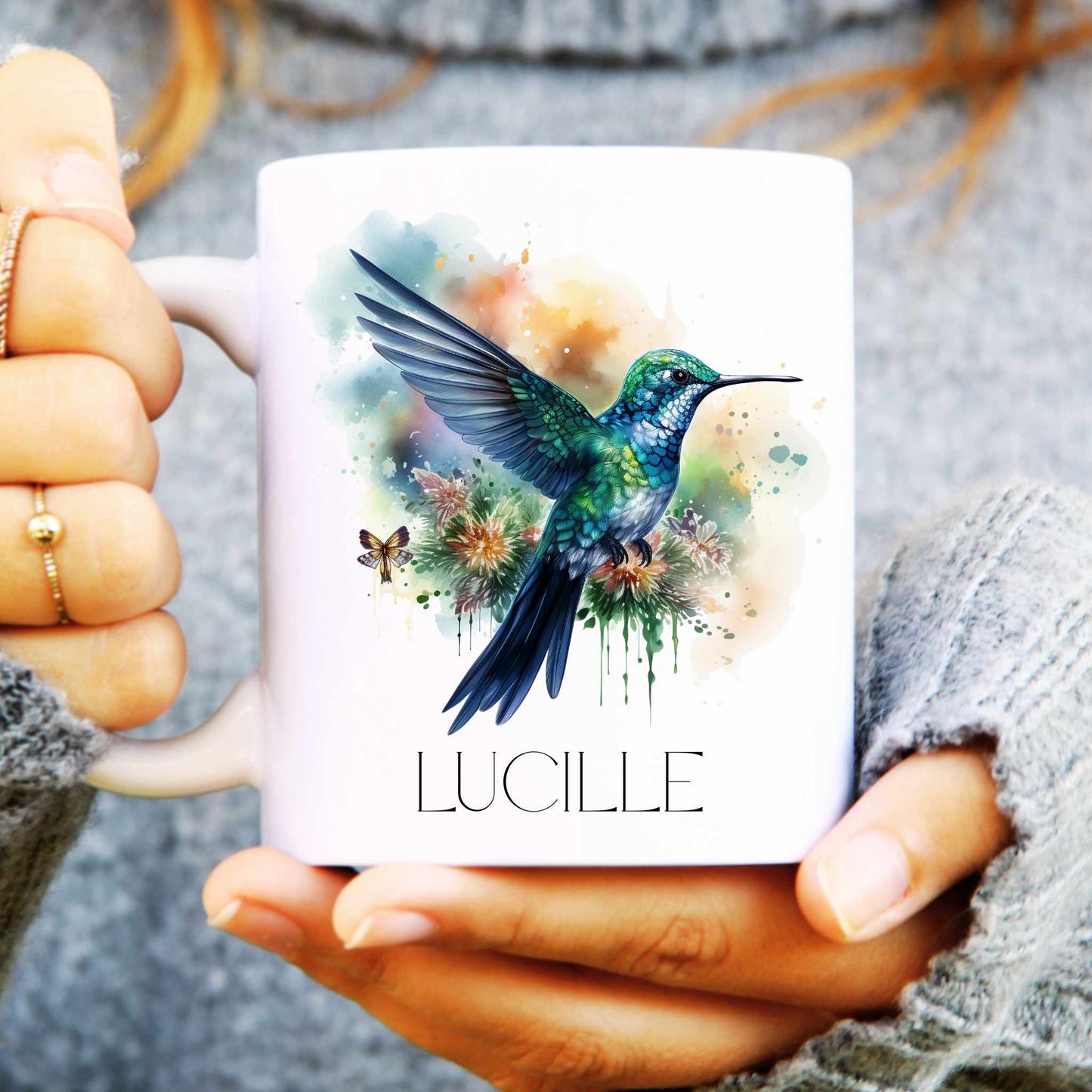 Person holding a mug with a colourful hummingbird design and 'LUCILLE' text.