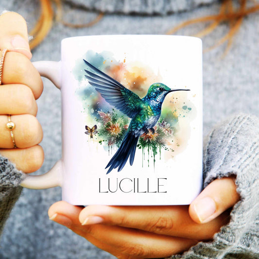 Person holding a mug with a colourful hummingbird design and 'LUCILLE' text.