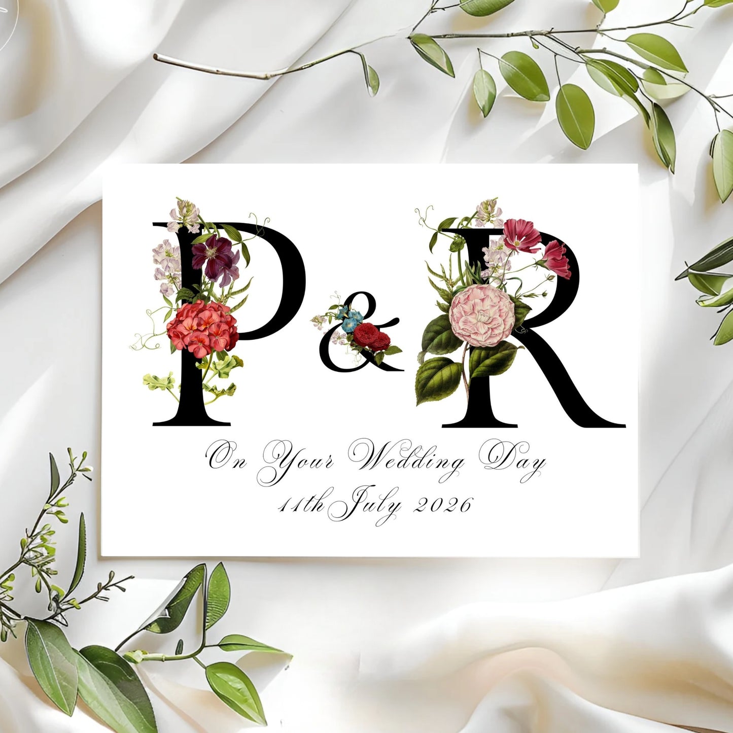 Wedding card with floral initials and date on a white fabric background